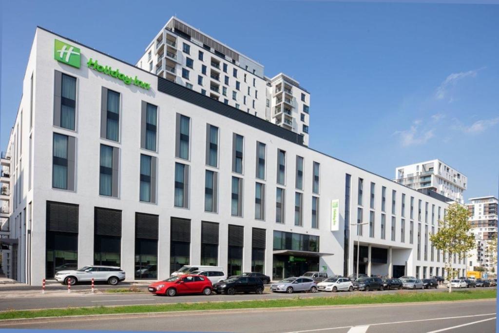 a white building with cars parked in a parking lot at Holiday Inn Düsseldorf City – Toulouser Allee, an IHG Hotel in Düsseldorf