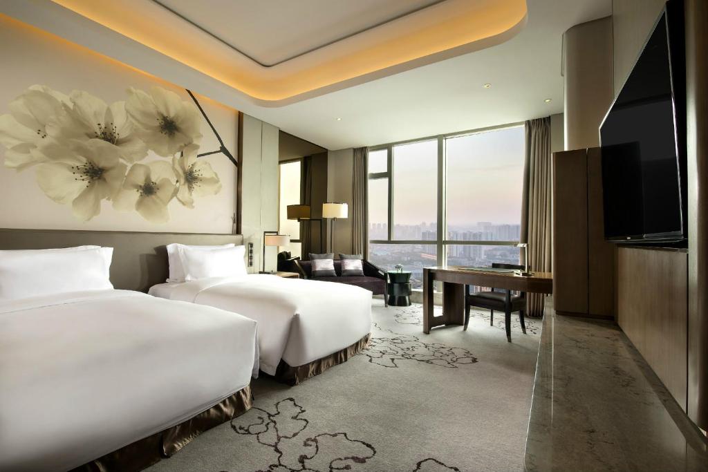 長沙市にあるKempinski Hotel Changshaのベッド2台、デスク、テレビが備わるホテルルームです。