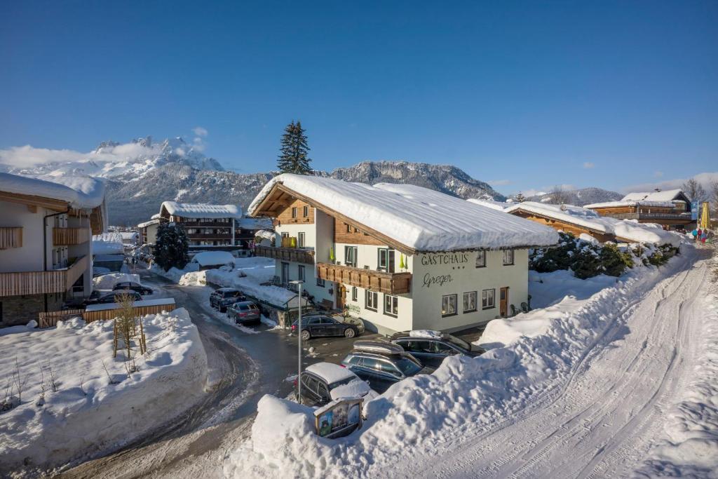 Gästehaus Greger في سانت جوهان في تيرول: مبنى مغطى بالثلج مع سيارات تقف في موقف للسيارات