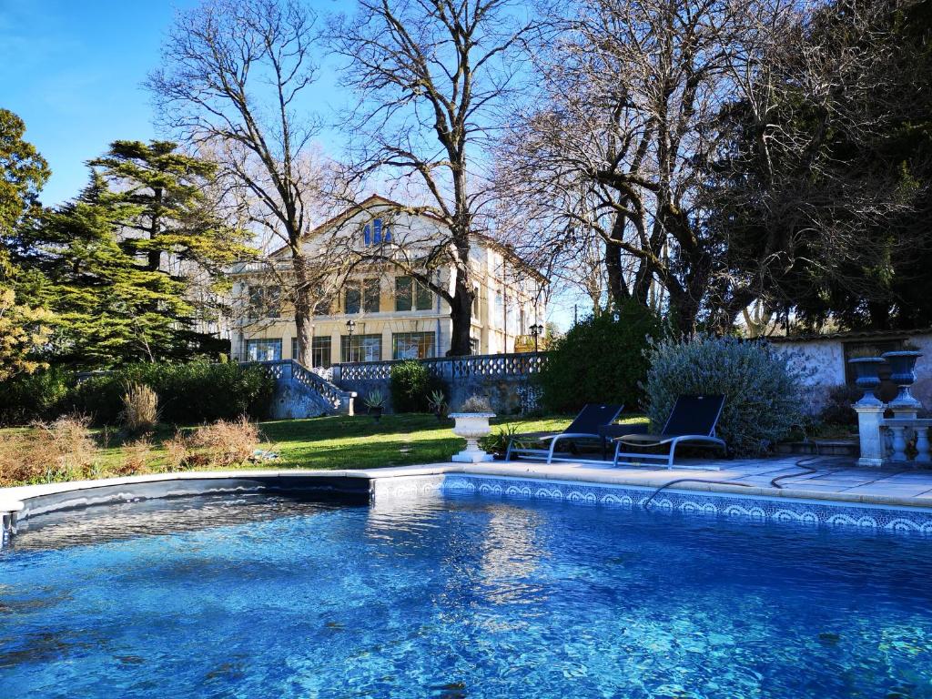 a swimming pool with two chairs in front of a house at Manoir le Roure in Châteauneuf-du-Rhône