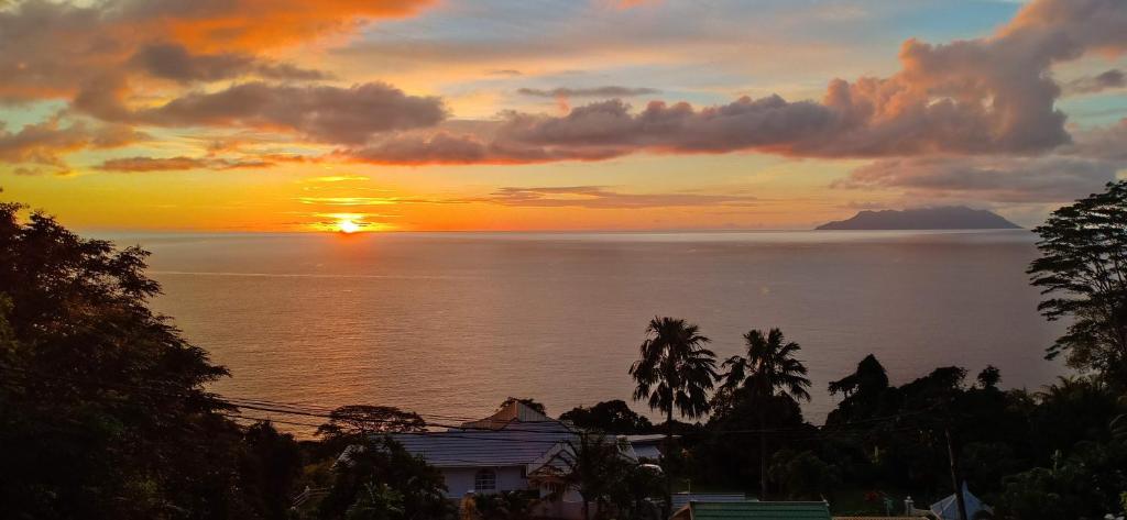 - un coucher de soleil sur l'océan avec une maison et des arbres dans l'établissement Reve Blêu, à Glacis