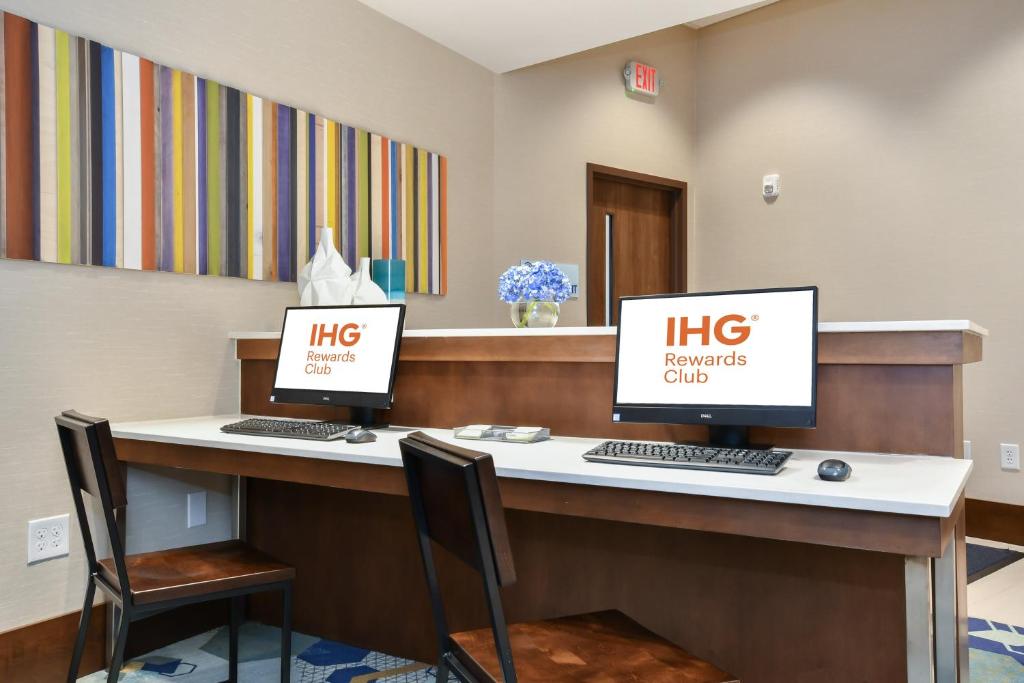 two computer monitors sitting on a desk in a waiting room at Holiday Inn Express & Suites Charlotte - Ballantyne by IHG in Charlotte