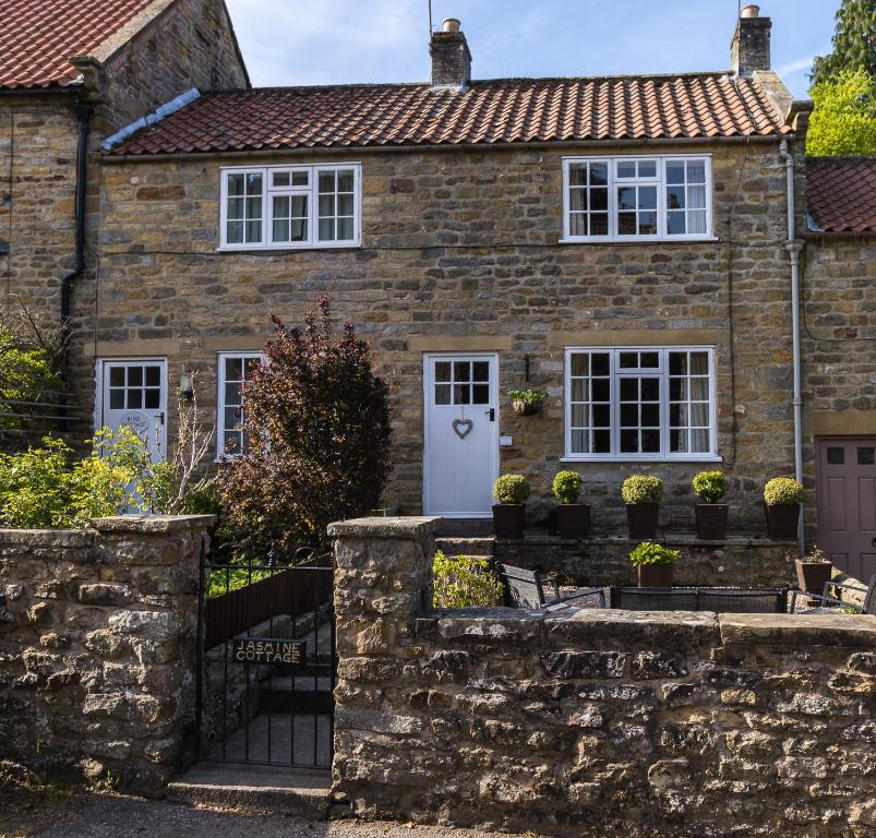 ein Steinhaus mit einer weißen Tür und Fenstern in der Unterkunft Jasmine Cottage Lastingham North Yorkshire in Pickering