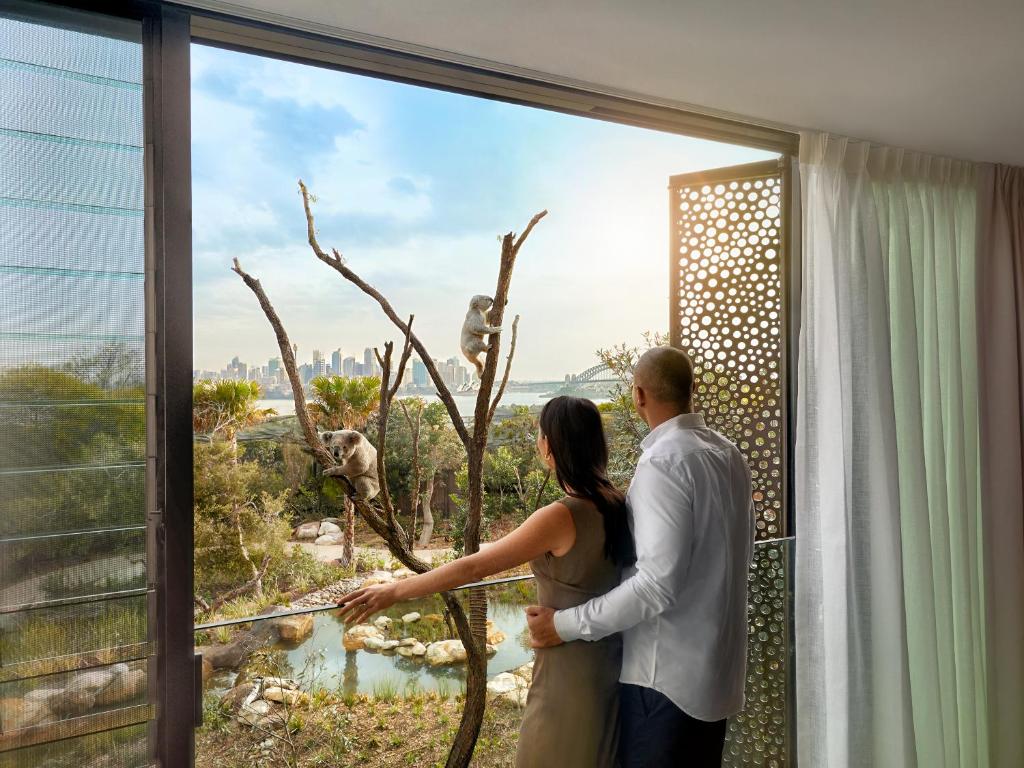 a man and woman looking out of a window at a giraffe at Wildlife Retreat at Taronga in Sydney