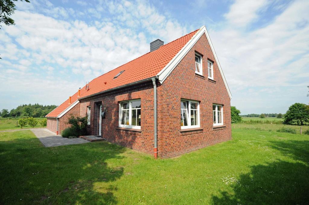 uma casa de tijolos com um telhado vermelho num campo em Ferienhaus Adamla, 65319 em Moormerland