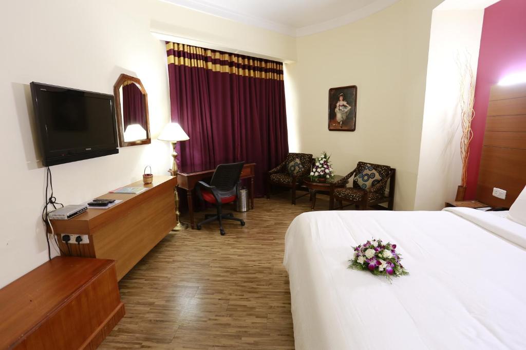 Habitación de hotel con cama, escritorio y TV. en Hotel Presidency, en Kochi