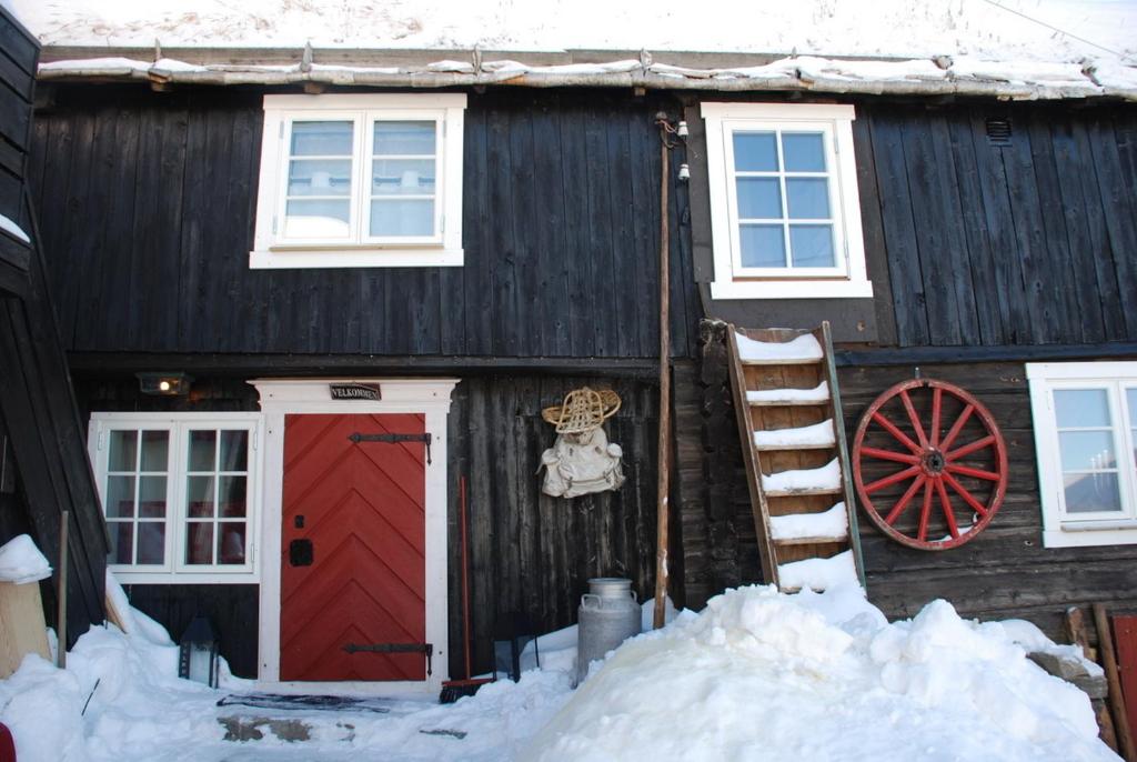 a black house with a red door and a ladder at Regnbuegården in Røros