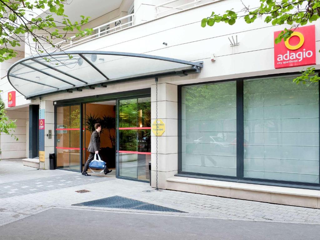 una mujer saliendo por la puerta de una tienda en Aparthotel Adagio La Défense Le Parc en Courbevoie