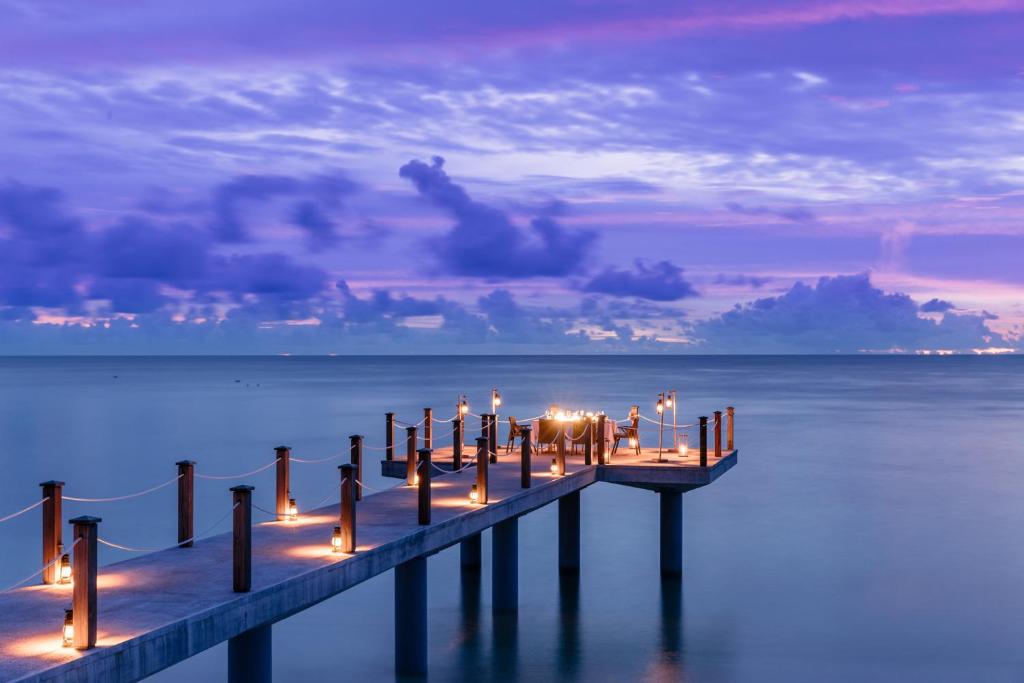 um cais com velas acesas na água à noite em Four Seasons Resort Seychelles at Desroches Island em Desroches