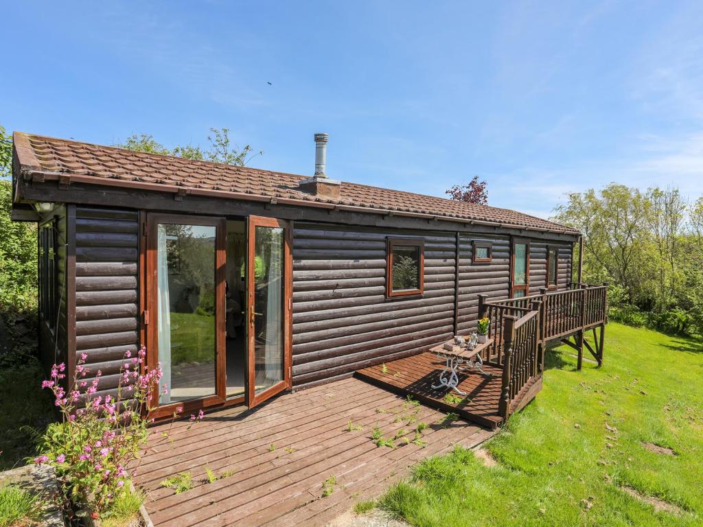 a log cabin with a deck in the grass at Castell Chalet in Pwllheli