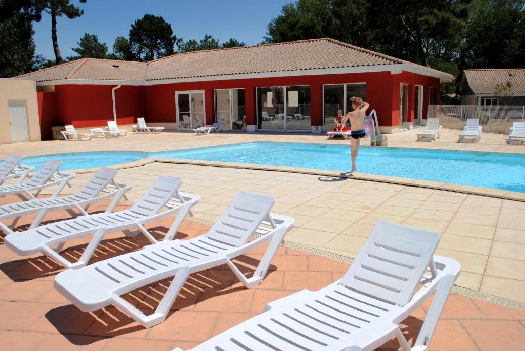 a woman standing next to a swimming pool with lounge chairs at Résidence Néméa Les Rives de Saint Brice in Arès