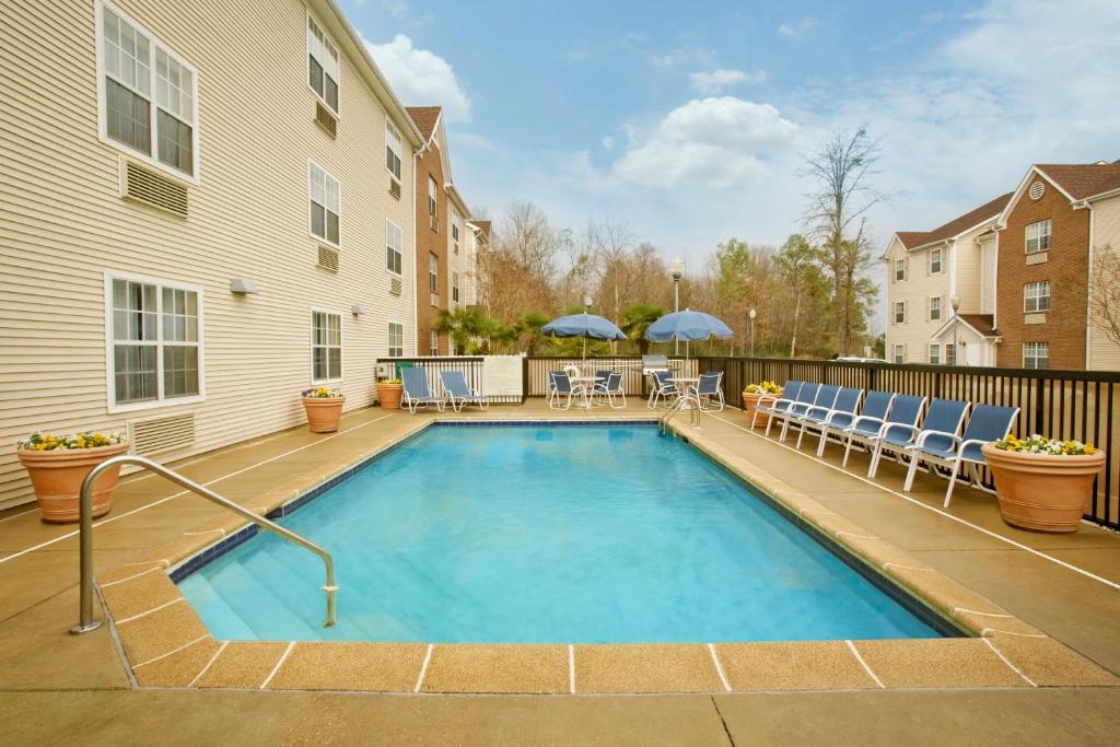 a swimming pool with chairs and tables and a building at Suburban Studios Jackson North in Jackson