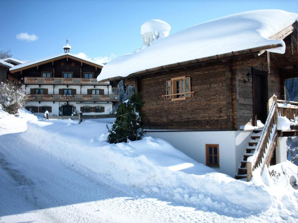 a house covered in snow with a building in the background at Viehhofbauer in Maria Alm am Steinernen Meer