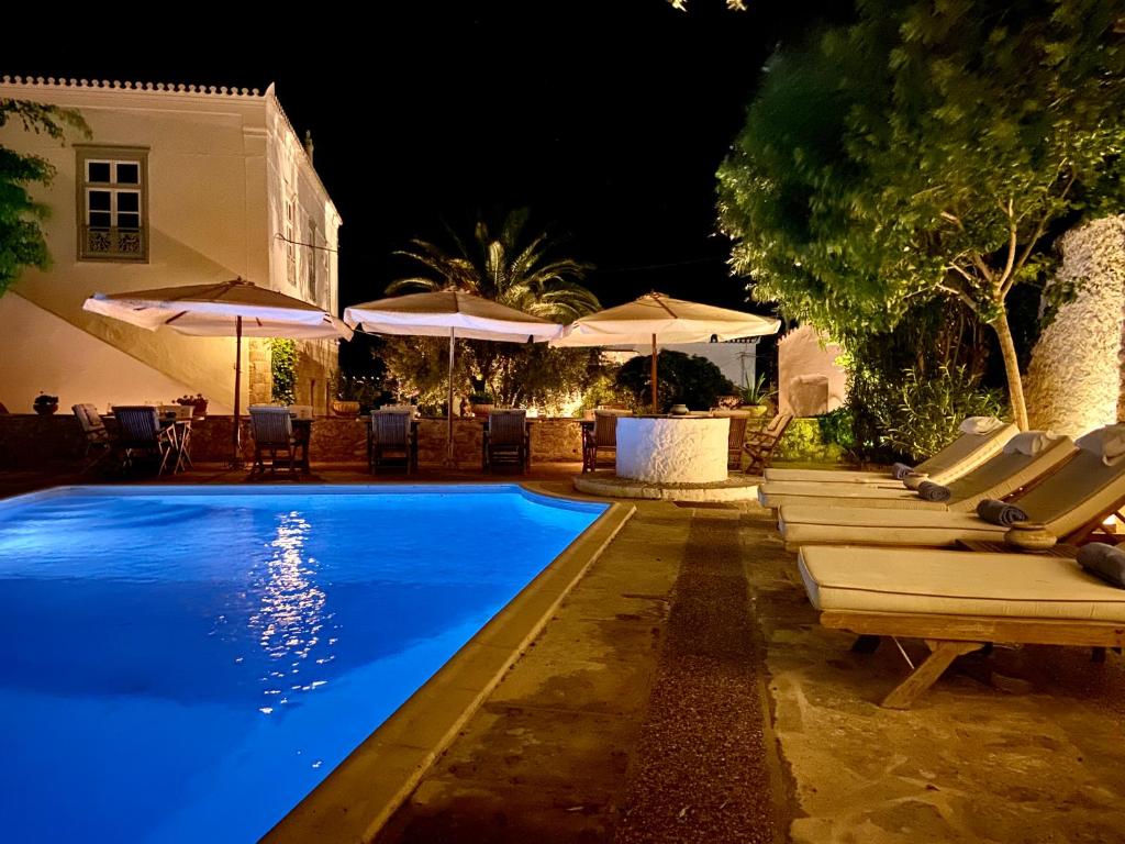 a pool with lounge chairs and umbrellas at night at Economou Mansion in Spetses