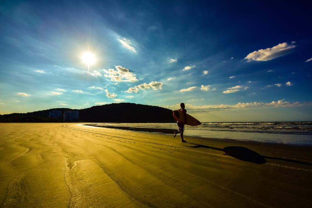 a man walking on the beach with a surfboard at Ap Riviera uma quadra da praia in Bertioga