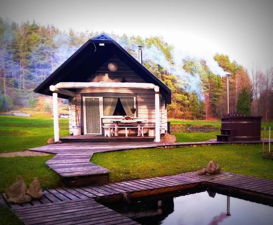 una pequeña cabaña con una terraza de madera junto a un estanque en White homestead, en Semeliškės