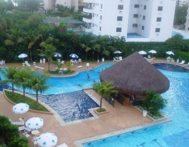 a swimming pool with a straw umbrella and a resort at Apartamento lazer na rua da praia in Riviera de São Lourenço