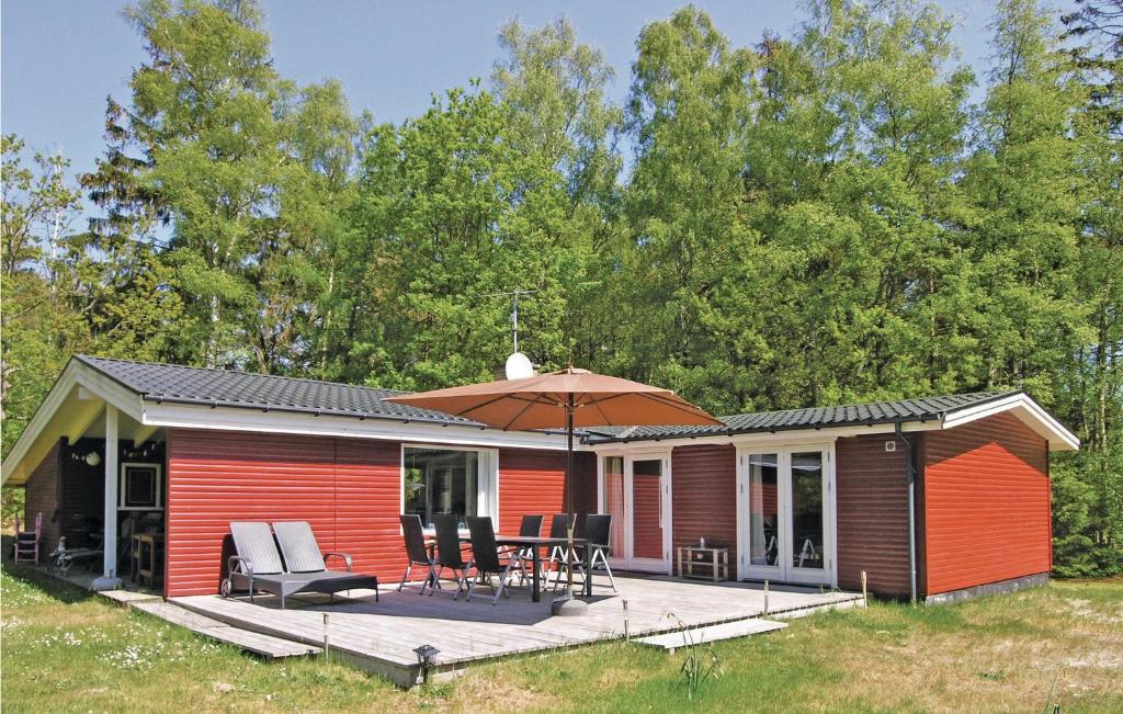 a red cabin with a deck and an umbrella at Holiday Home Brogårdsvejen Nexø X in Bedegård