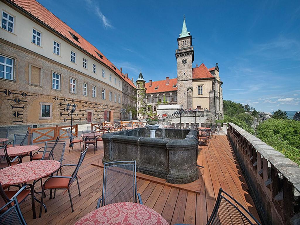 un patio al aire libre con mesas y sillas y una torre del reloj en EA Zamecky Hotel Hruba Skala en Hrubá Skála