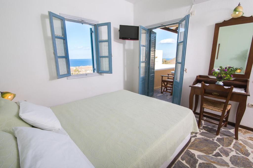 a bedroom with a bed and a desk and windows at Anemoessa Villa in Oia