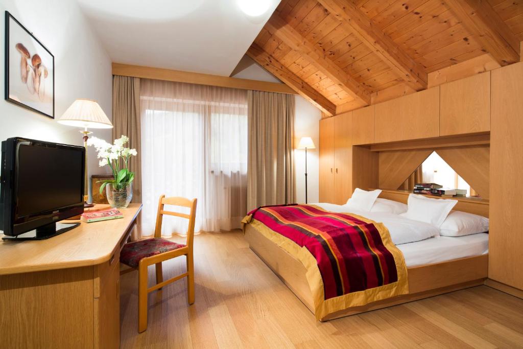 a bedroom with a bed and a desk with a television at Ciasa Roby in San Cassiano