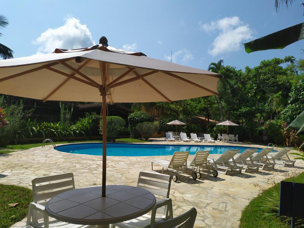 a table with an umbrella next to a pool at Chalé Pousada da Aldeia in Boicucanga