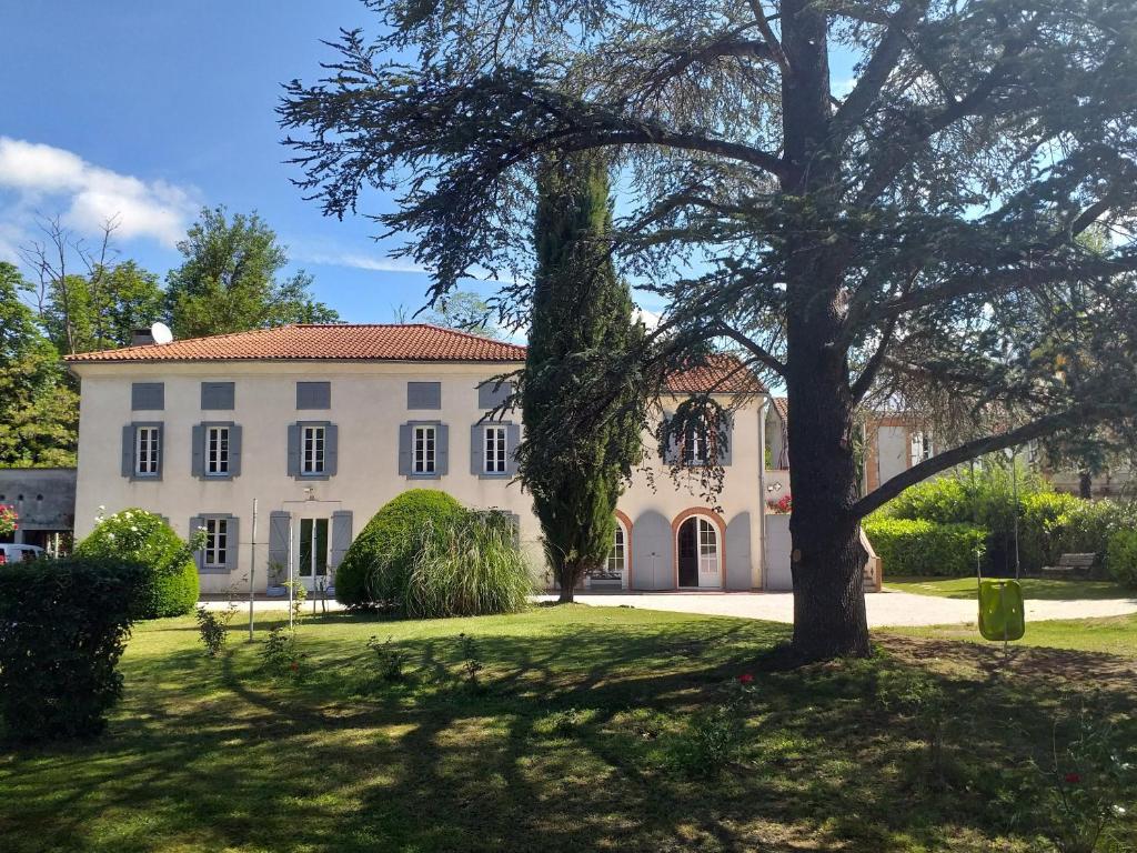 una grande casa bianca con un albero in primo piano di Chez Celine et Philippe appartement dans propriété de charme avec piscine a Le Fossat