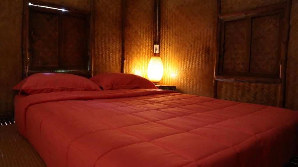 - une chambre avec un grand lit et une couette rouge dans l'établissement บ้านไร่ชายทุ่ง, à Kanchanaburi