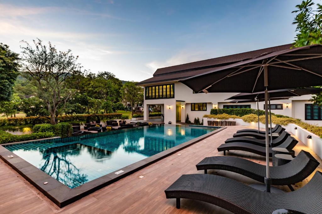 - une piscine avec des chaises et un parasol dans l'établissement Merchant Villa- SHA Extra Plus, à Chiang Mai