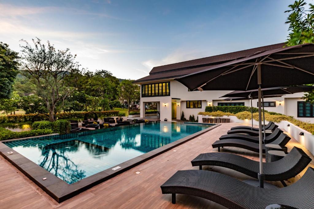 a swimming pool with chairs and an umbrella at Merchant Villa- SHA Extra Plus in Chiang Mai