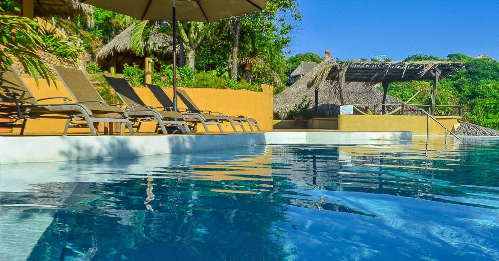 a swimming pool with chairs and an umbrella and water at OceanoMar in Mazunte