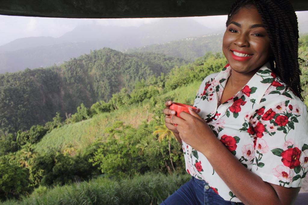 a woman smiling while holding a cup in a valley at Matthew's Miracle View in Roseau