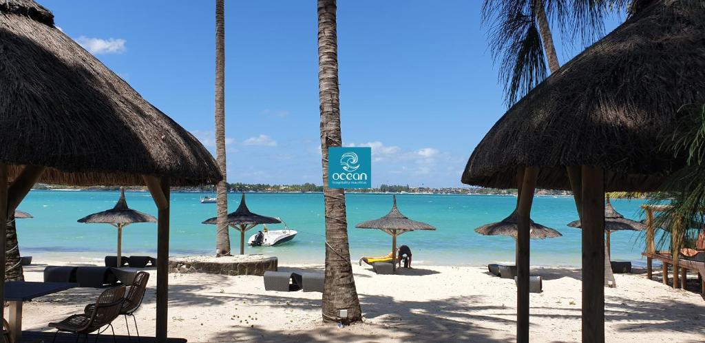 uma praia com alguns guarda-sóis de palha e o oceano em Ocean Villas Hotel em Grand Baie