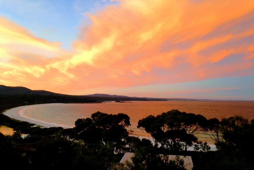 a sunset over a beach with trees in the foreground at DOLPHIN LOOKOUT COTTAGE - amazing views of the Bay of Fires in Binalong Bay