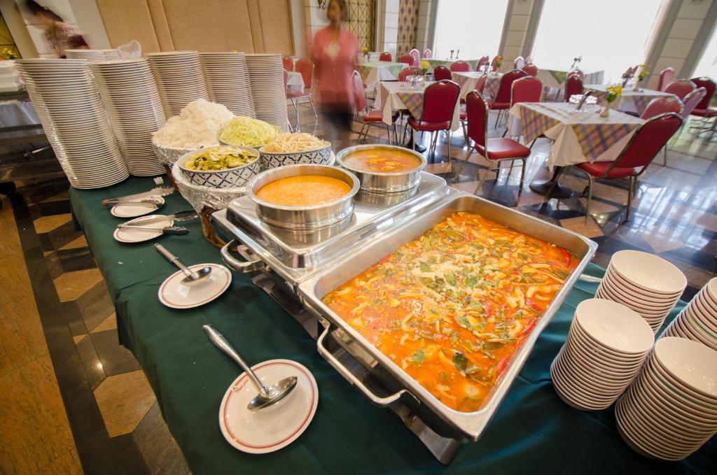 A buffet station with curry-style dishes, rice, noodles and stacks of plates.