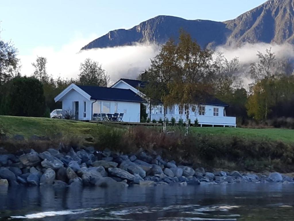una casa junto a un río con montañas en el fondo en feriehus ved sjøen en Tomrefjord
