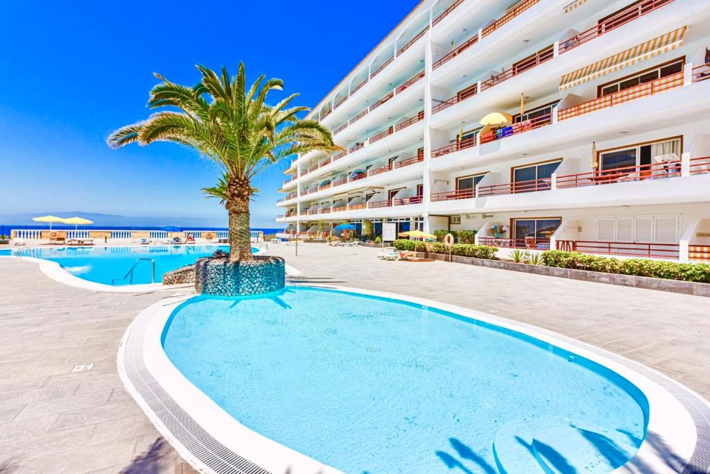 a swimming pool with a palm tree in front of a building at Апартаменты Playa de la Arena in Puerto de Santiago