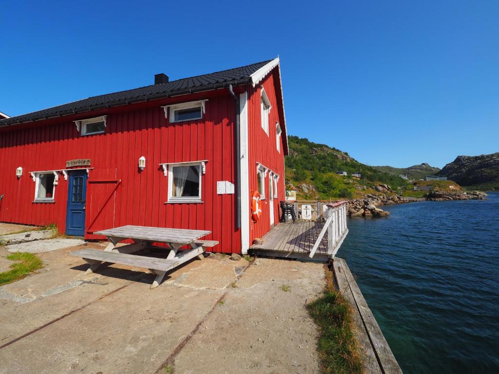 un edificio rojo con un banco junto a un cuerpo de agua en Lofoten Troll Point, en Bøstad