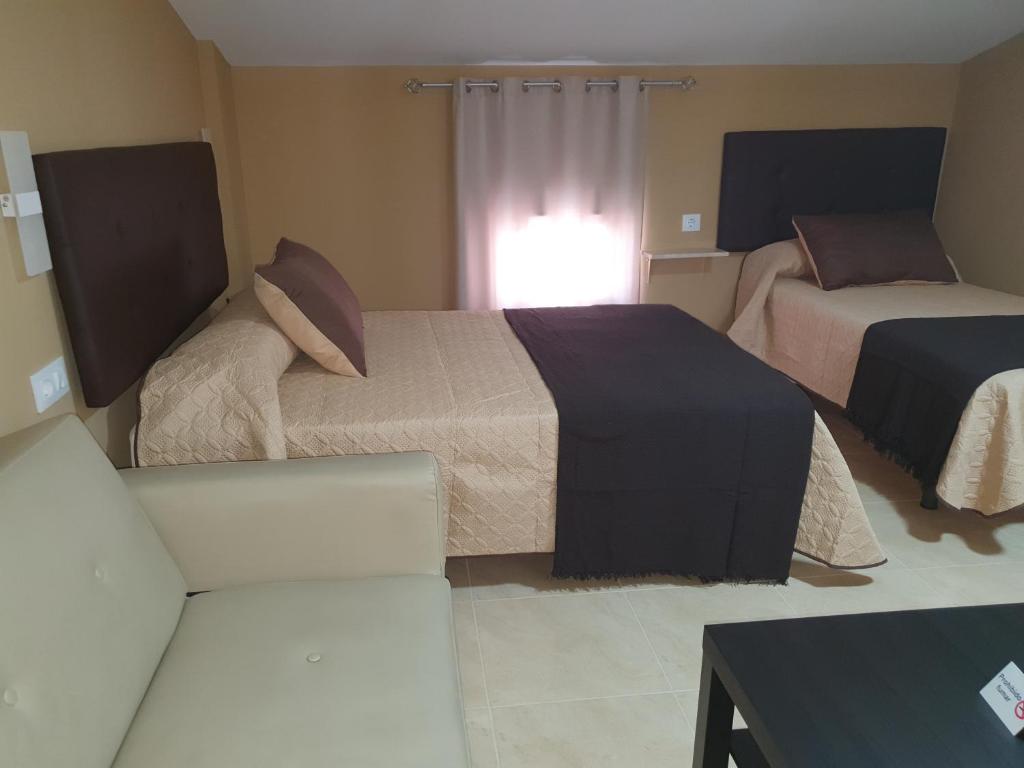 a hotel room with two beds and a couch at Hostal Málaga in Arcos de la Frontera