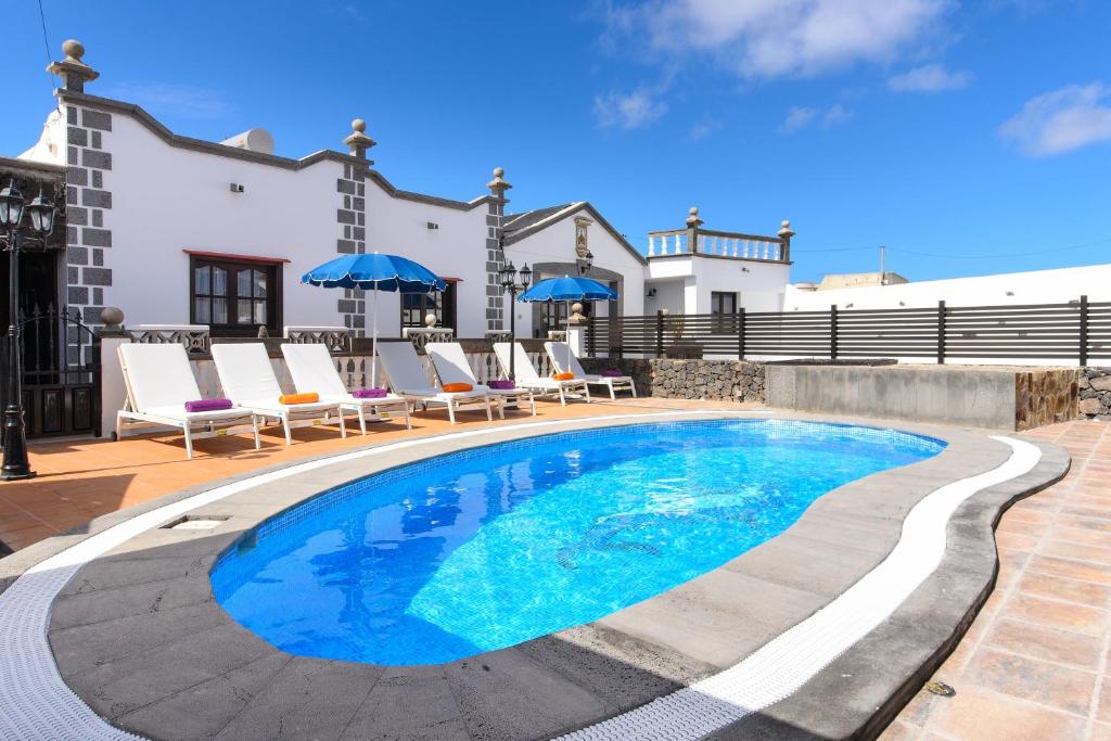 a swimming pool in front of a house with chairs and umbrellas at Villa Las Calderetas in Tinguatón