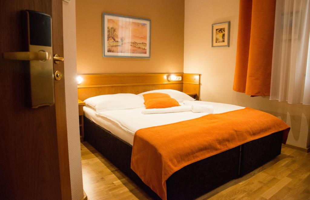a bedroom with a bed with an orange blanket on it at Hotel Wagner in Szombathely