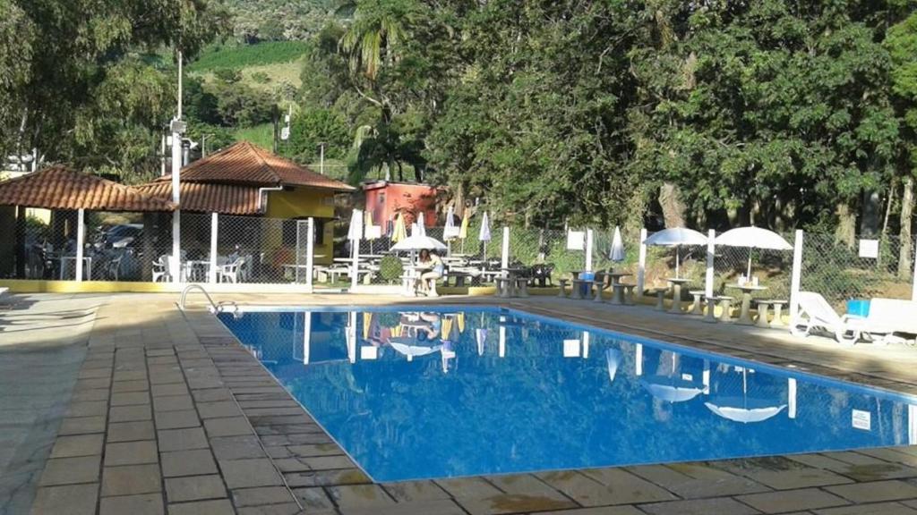 a blue swimming pool with chairs and umbrellas next to at Camping e Pousada Paiol in Águas da Prata