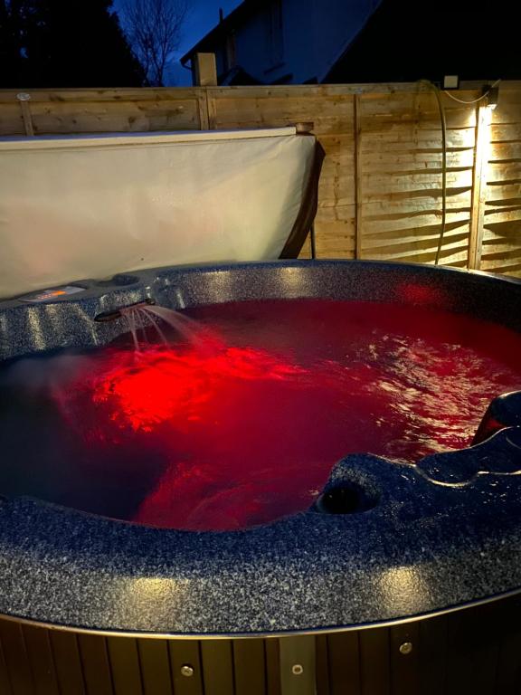 GROOMS COTTAGE OUTSIDE HOT TUB في Beith: حوض استحمام ساخن ممتلئ بالماء الأحمر في الليل