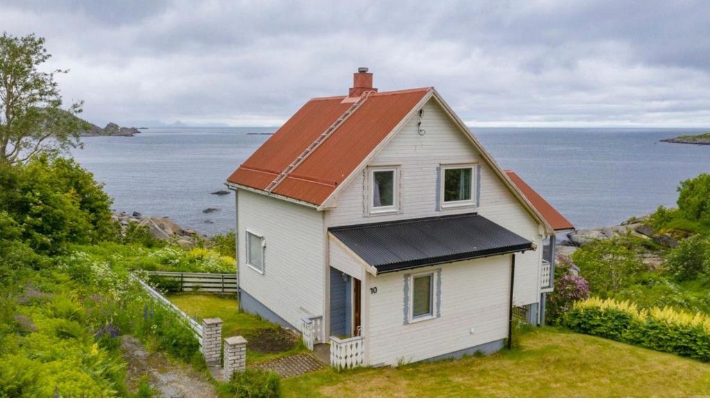 a white house with an orange roof next to the ocean at House by the sea Reine, Lofoten in Reine