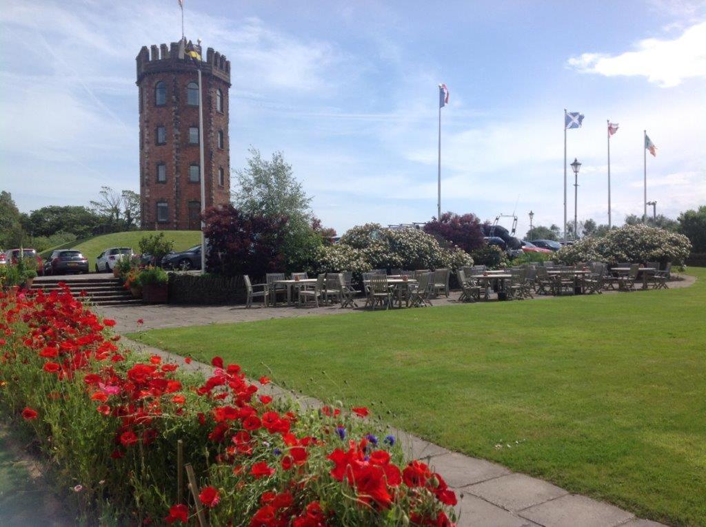 uma torre do relógio com mesas e flores num parque em Towers Hotel & Spa em Swansea
