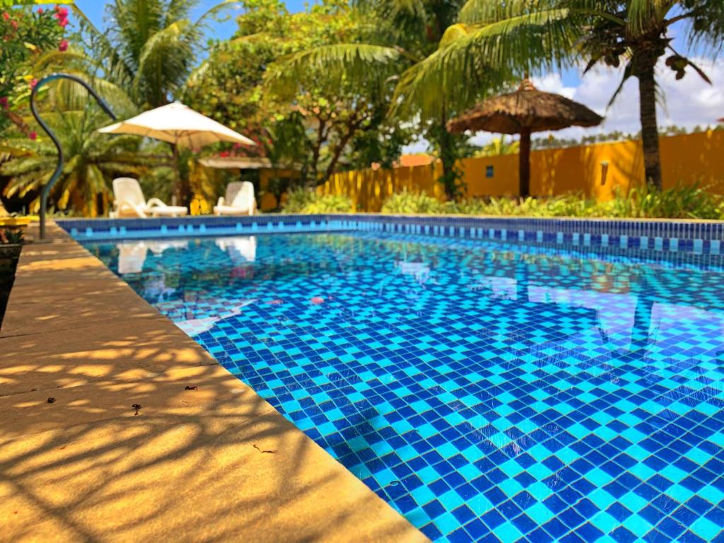 a blue tile swimming pool with umbrellas at Pousada Costeira da Barra in Maragogi