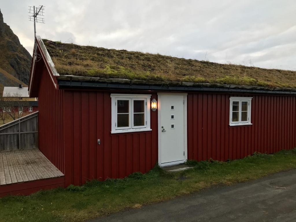 a red building with a grass roof with a white door at Eggum Fishermans Cabin in Bøstad