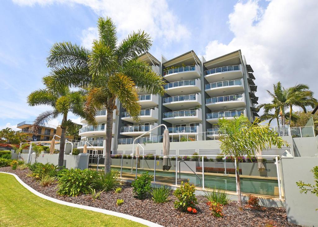 un gran edificio blanco con palmeras delante en Tingeera Bespoke Beachfront Apartments, en Hervey Bay