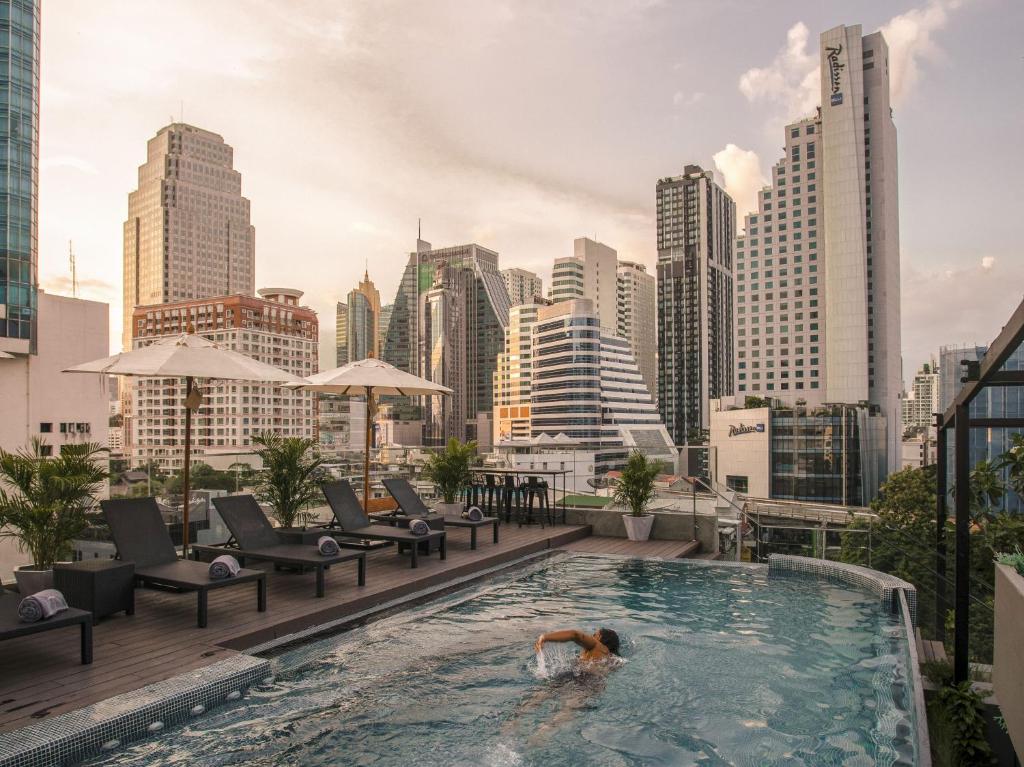 un hombre nadando en una piscina en lo alto de un perfil urbano en Tastoria Collection Sukhumvit - SHA Extra Plus en Bangkok