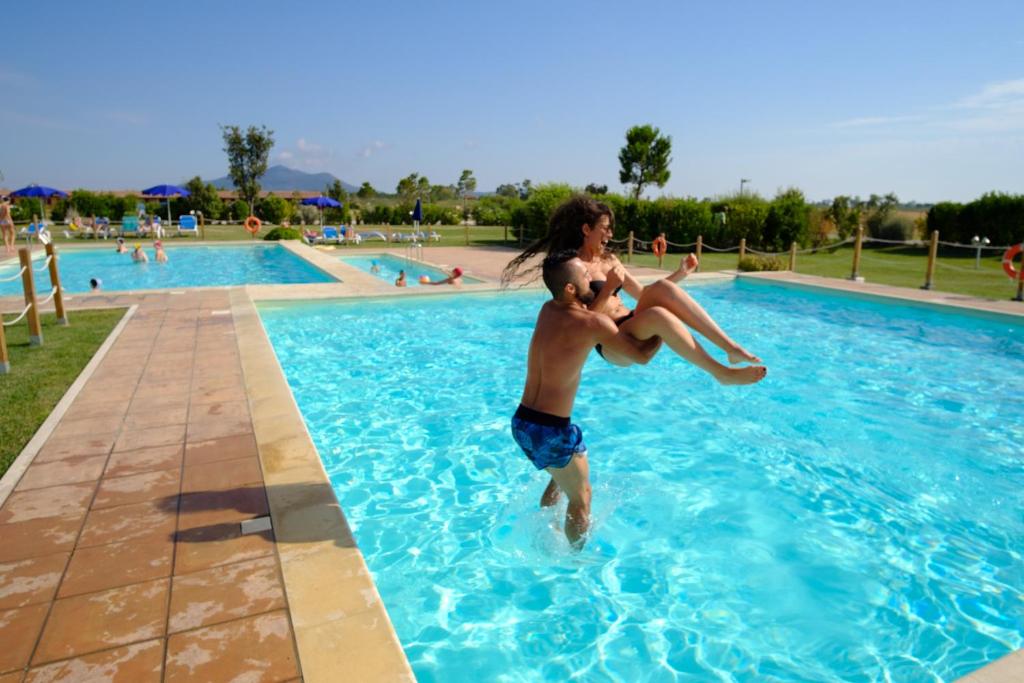 a man and woman jumping into a swimming pool at Residenza Principina in Principina Terra